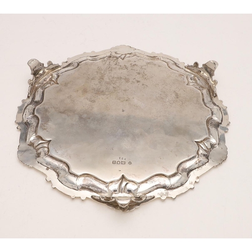 233 - A LATE VICTORIAN SALVER. shaped circular outline, with a husk & scroll border and raised on three le... 