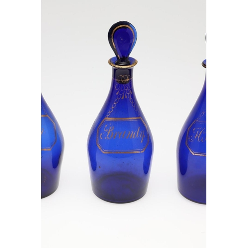 1504 - A SET OF THREE REGENCY BLUE GLASS DECANTERS. each with faux gilt labels for Rum, Brandy and Hollands... 