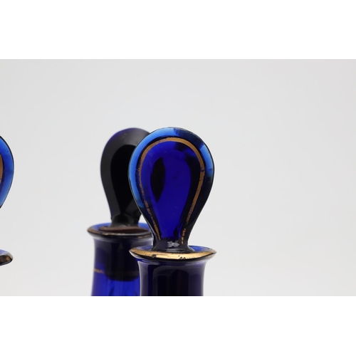 1504 - A SET OF THREE REGENCY BLUE GLASS DECANTERS. each with faux gilt labels for Rum, Brandy and Hollands... 