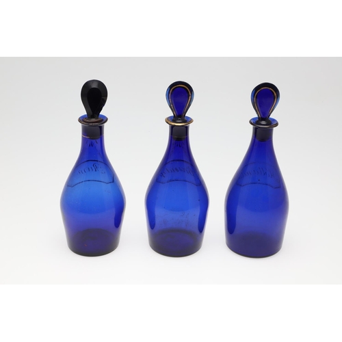 1504 - A SET OF THREE REGENCY BLUE GLASS DECANTERS. each with faux gilt labels for Rum, Brandy and Hollands... 