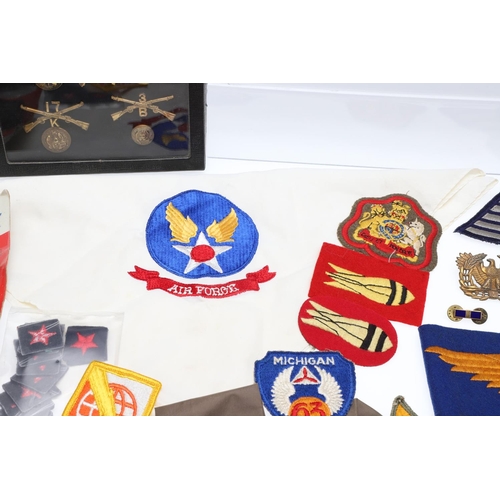 265 - A COLLECTION OF AMERICAN HAT INSIGNIA AND OTHER BADGES AND PATCHES. A mounted collection of crossed ... 