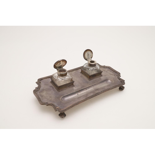 115 - A GEORGE V SILVER INKSTAND. of shaped rectangular outline, with a moulded border, fitted with two no... 