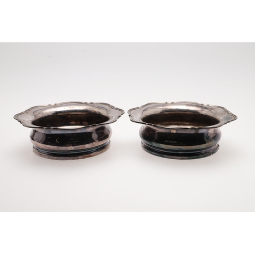 187 - A PAIR OF EARLY 20TH CENTURY SILVER MOUNTED WINE COASTERS. shaped circular outline, with a moulded b... 