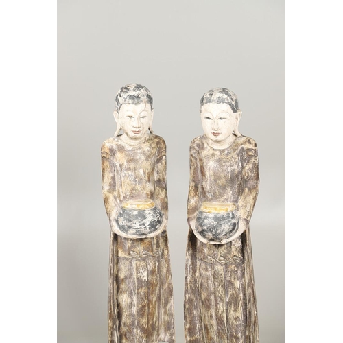 1203 - A PAIR OF THAI POLYCHROME CARVED STANDING WOODEN FIGURES OF MONKS. 20th century, each holding an off... 