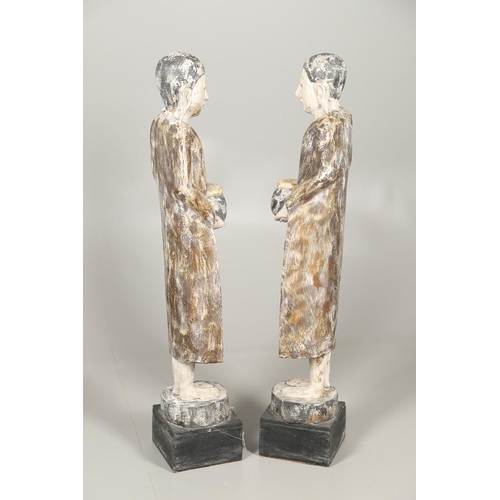 1203 - A PAIR OF THAI POLYCHROME CARVED STANDING WOODEN FIGURES OF MONKS. 20th century, each holding an off... 