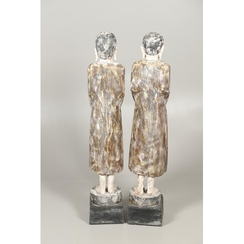 1203 - A PAIR OF THAI POLYCHROME CARVED STANDING WOODEN FIGURES OF MONKS. 20th century, each holding an off... 