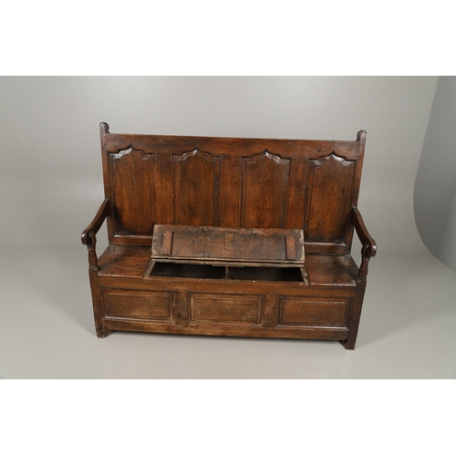 1307 - AN 18TH CENTURY OAK BOX SETTLE. the quadruple panelled back with carved arch ogee detail over a hing... 