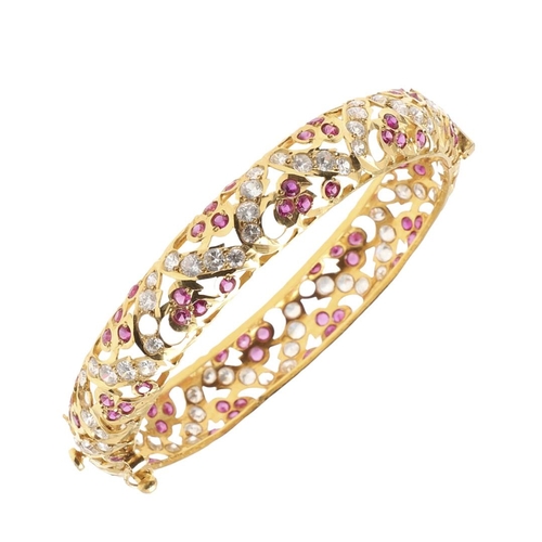 1053 - A 22CT GOLD AND GEM SET HINGED BANGLE. of openwork design, mounted with circular-cut rubies and circ... 