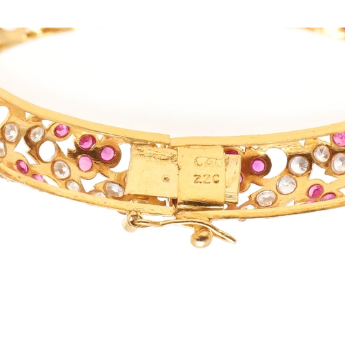 1053 - A 22CT GOLD AND GEM SET HINGED BANGLE. of openwork design, mounted with circular-cut rubies and circ... 