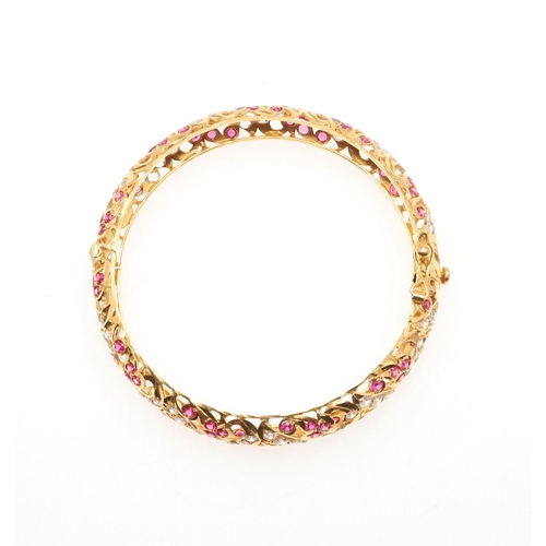 1053 - A 22CT GOLD AND GEM SET HINGED BANGLE. of openwork design, mounted with circular-cut rubies and circ... 