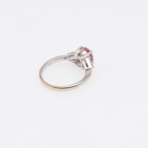 1062 - A PINK SAPPHIRE AND DIAMOND THREE STONE RING. the oval-shaped pink sapphire is set with two triangul... 