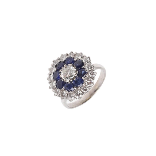 1076 - A SAPPHIRE AND DIAMOND CLUSTER RING. centred with a circular-cut diamond, within a surround of circu... 