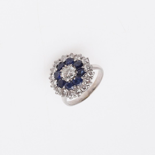 1076 - A SAPPHIRE AND DIAMOND CLUSTER RING. centred with a circular-cut diamond, within a surround of circu... 