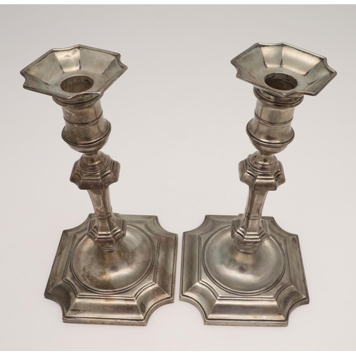 157 - A PAIR OF GEORGE V SILVER CANDLESTICKS. on canted square bases (loaded), with spool-shaped capitals,... 