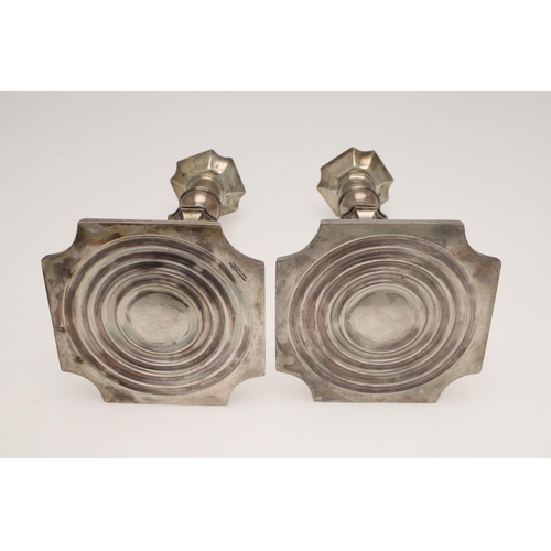 157 - A PAIR OF GEORGE V SILVER CANDLESTICKS. on canted square bases (loaded), with spool-shaped capitals,... 