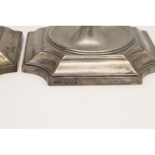 157 - A PAIR OF GEORGE V SILVER CANDLESTICKS. on canted square bases (loaded), with spool-shaped capitals,... 