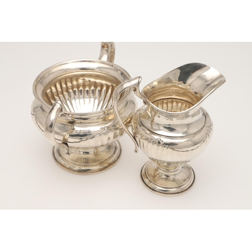 47 - A GEORGE V FOUR-PIECE SILVER TEA SET. of circular form, with scroll handle, decorated around the low... 