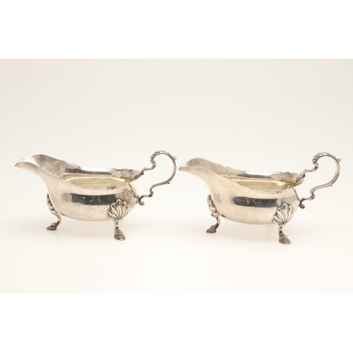 44 - A PAIR OF SILVER SAUCE BOATS. With card cut border, scroll handle and stood on three hoofed feet. Ha... 