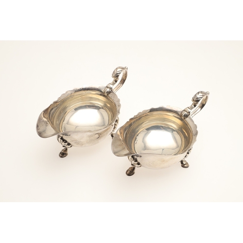 44 - A PAIR OF SILVER SAUCE BOATS. With card cut border, scroll handle and stood on three hoofed feet. Ha... 