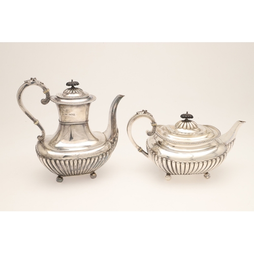 51 - AN EDWARDIAN SILVER FOUR PIECE TEA SET. Of half fluted oval form with scroll handles, gadrooned bord... 