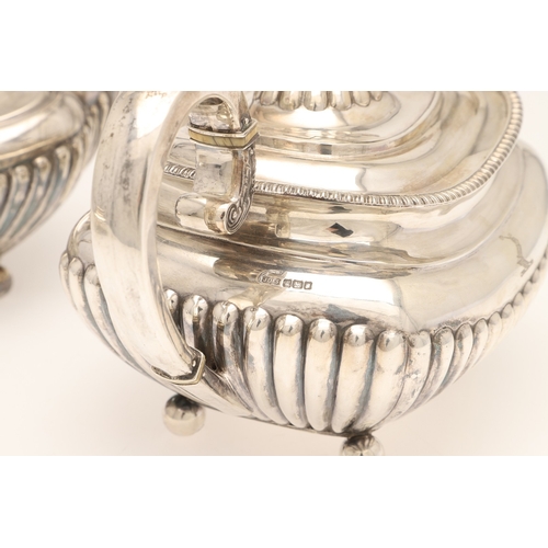51 - AN EDWARDIAN SILVER FOUR PIECE TEA SET. Of half fluted oval form with scroll handles, gadrooned bord... 