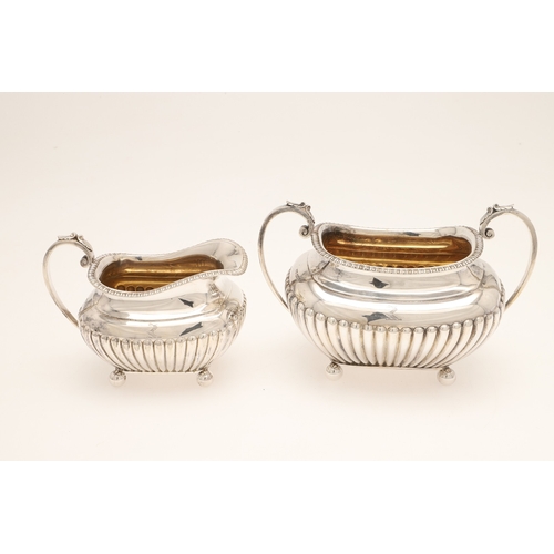 51 - AN EDWARDIAN SILVER FOUR PIECE TEA SET. Of half fluted oval form with scroll handles, gadrooned bord... 