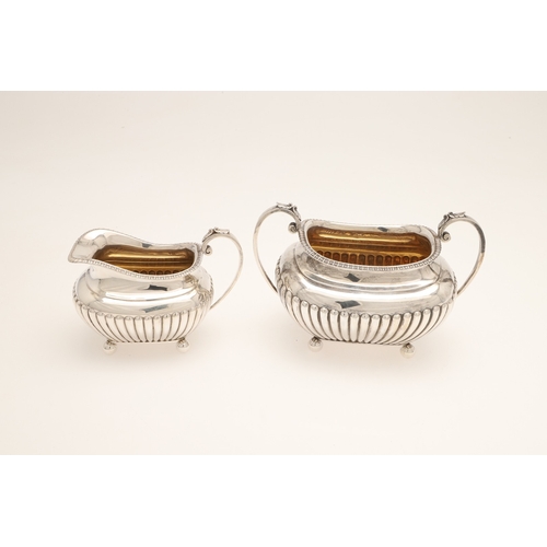 51 - AN EDWARDIAN SILVER FOUR PIECE TEA SET. Of half fluted oval form with scroll handles, gadrooned bord... 