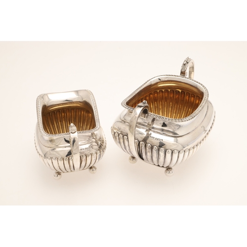 51 - AN EDWARDIAN SILVER FOUR PIECE TEA SET. Of half fluted oval form with scroll handles, gadrooned bord... 