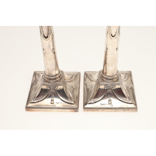 68 - A PAIR OF EDWARDIAN SILVER CANDLESTICKS OF CORINTHIAN COLUMN FORM. Hung swags & ribbons on gadrooned... 