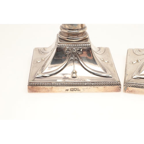 68 - A PAIR OF EDWARDIAN SILVER CANDLESTICKS OF CORINTHIAN COLUMN FORM. Hung swags & ribbons on gadrooned... 