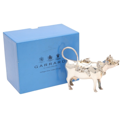 78 - A SILVER COW CREAMER BY GARRARD & CO LTD. The cow decorated with floral wreaths and insect to the li... 