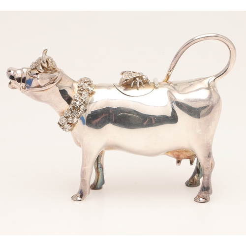 78 - A SILVER COW CREAMER BY GARRARD & CO LTD. The cow decorated with floral wreaths and insect to the li... 