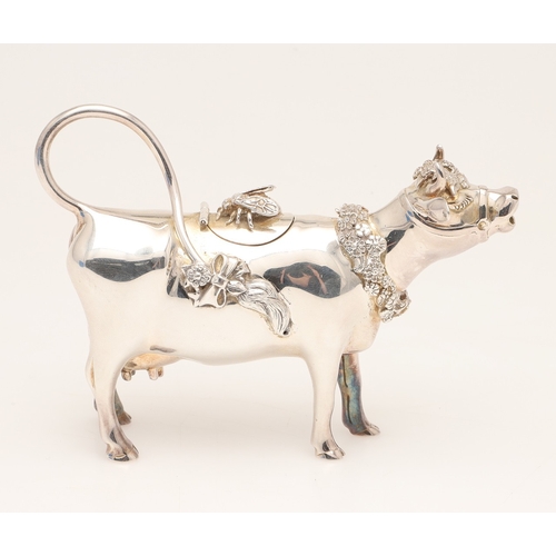 78 - A SILVER COW CREAMER BY GARRARD & CO LTD. The cow decorated with floral wreaths and insect to the li... 