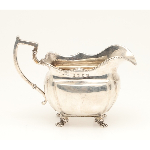 83 - A GEORGE III IRISH SILVER CREAM JUG. With gadrooned rim and stood on paw feet, engraved initials A &... 