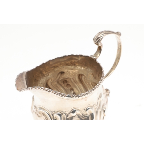 30 - A GEORGE III CREAM JUG. With scroll handle, repousse and gadrooned decoration and a blank cartouche,... 