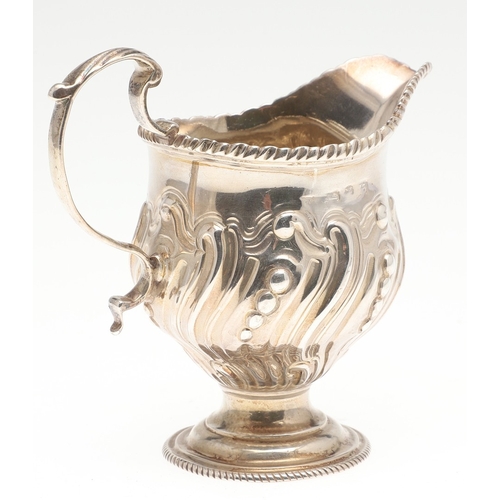 30 - A GEORGE III CREAM JUG. With scroll handle, repousse and gadrooned decoration and a blank cartouche,... 