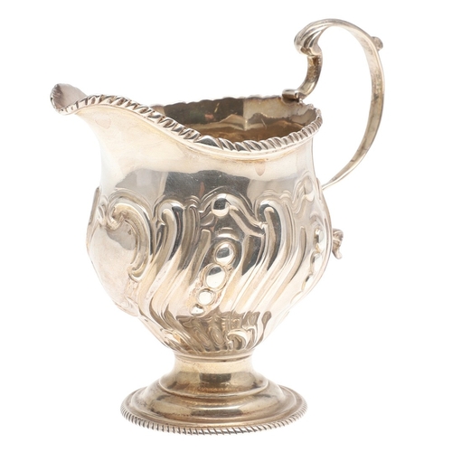 30 - A GEORGE III CREAM JUG. With scroll handle, repousse and gadrooned decoration and a blank cartouche,... 