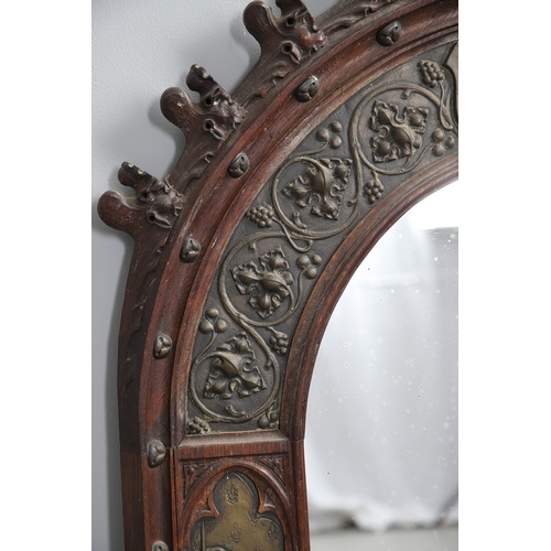 543 - A LATE 19TH CENTURY 'GOTHIC' OAK AND BRASS WALL MIRROR. the carved arched surround to pressed brass ... 