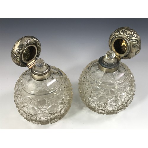 3352 - PAIR OF CUT GLASS SILVER TOP PERFUME BOTTLES EACH APPROX. 14 cms WITH REPOUSSE DECORATED HINGED SILV... 