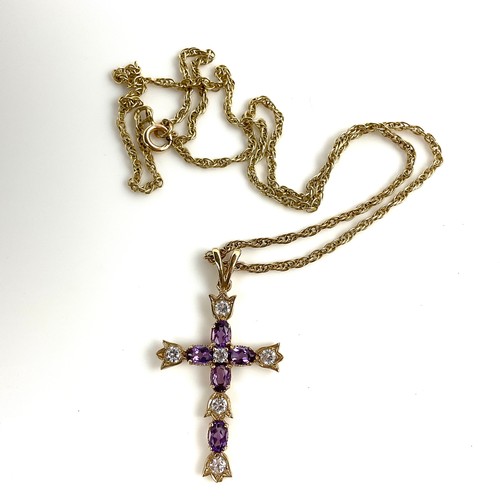 599 - 9 CT. GOLD CRUCIFIX SET WITH PURPLE AND WHITE STONES ON A 9 CT. GOLD NECKLACE