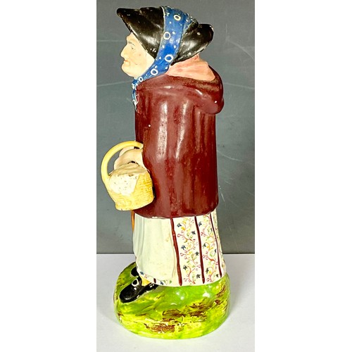 141 - EARLY 19TH STAFFORDSHIRE FIGURE OF OLD WOMAN WEARING A CLOAK WITH BASKET AND STICK