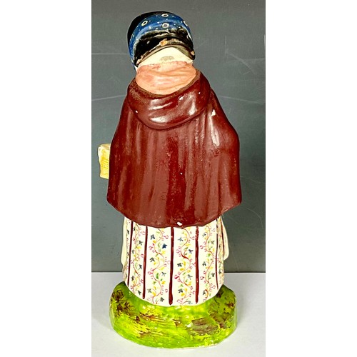 141 - EARLY 19TH STAFFORDSHIRE FIGURE OF OLD WOMAN WEARING A CLOAK WITH BASKET AND STICK