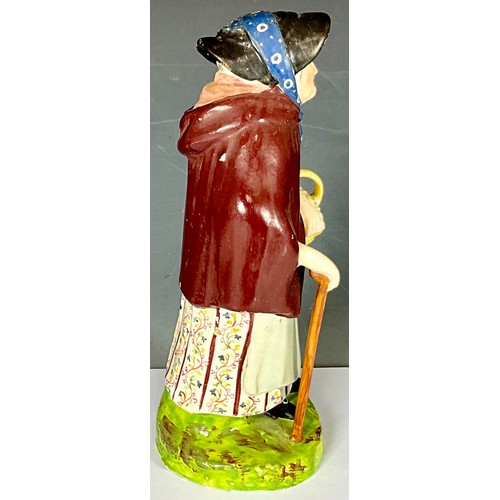 141 - EARLY 19TH STAFFORDSHIRE FIGURE OF OLD WOMAN WEARING A CLOAK WITH BASKET AND STICK