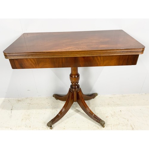 563 - MAHOGANY CARD TABLE ON TURNED PEDESTAL WITH FOUR UPTURNED FLUTED LEGS AND CASTERS