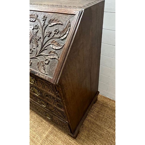 115 - A heavy carved bureau, the fall front enclosing interior fitted drawers and pigeon holes with four l... 