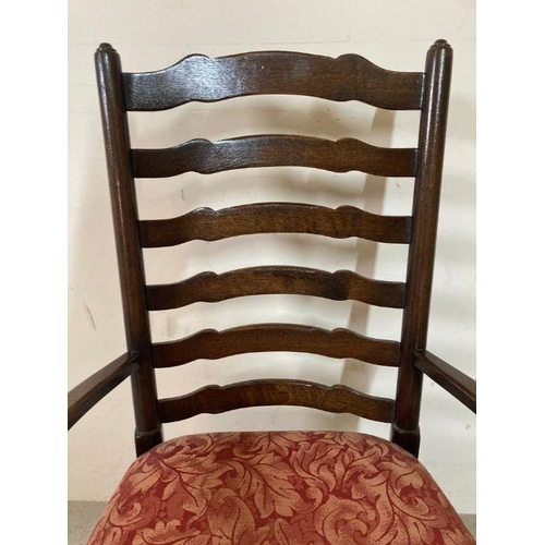 176 - An oak spool turned ladder back arm chair upholstered in red