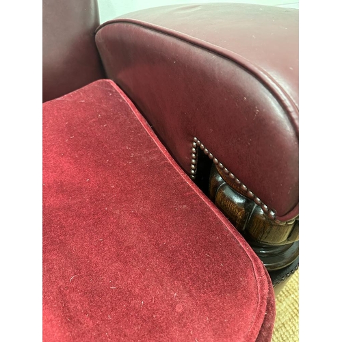 208 - A two seater faux leather oxblood sofa with carved oak arm supports and two matching chairs