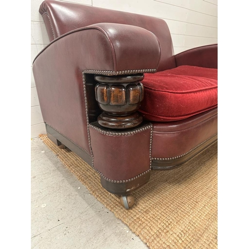 208 - A two seater faux leather oxblood sofa with carved oak arm supports and two matching chairs