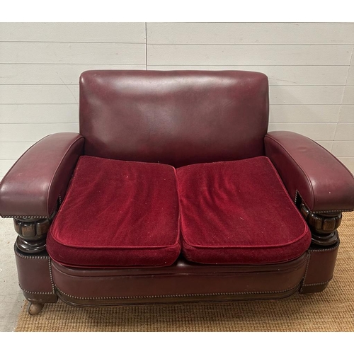 208 - A two seater faux leather oxblood sofa with carved oak arm supports and two matching chairs