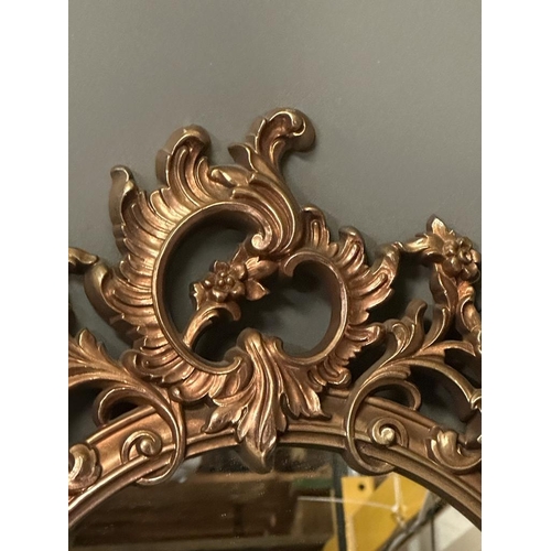 277 - A wooden framed gold painted oval wall hanging mirror in the Rococo style (49cm x 73cm)